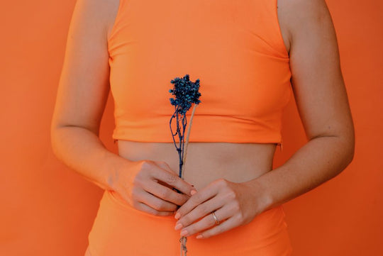 girl in orange workout set holding a flower near her stomach