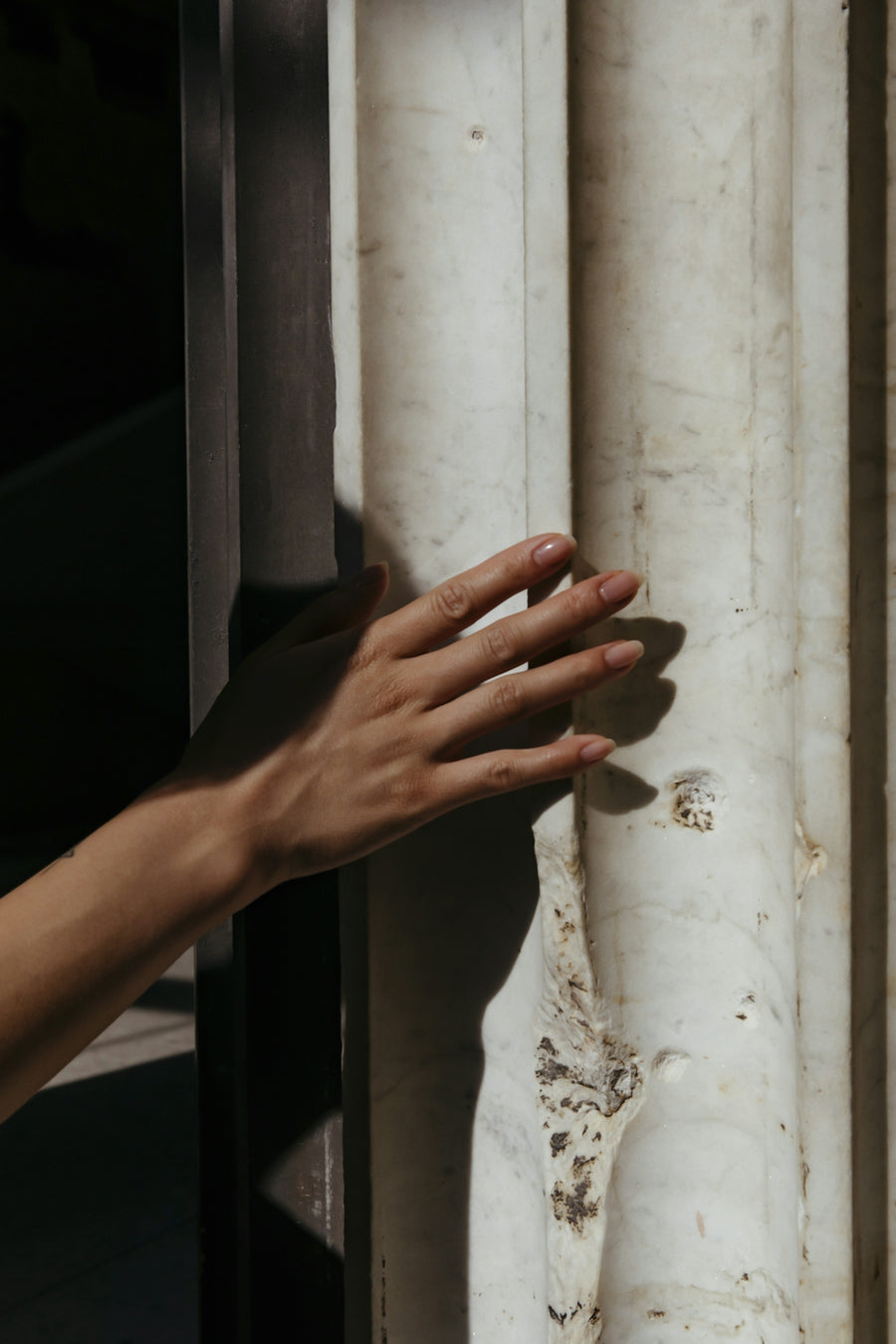 A hand gently touching a textured, sunlit marble surface.