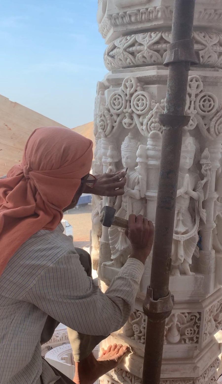 Artisan intricately carving stone sculptures on a decorative pillar.