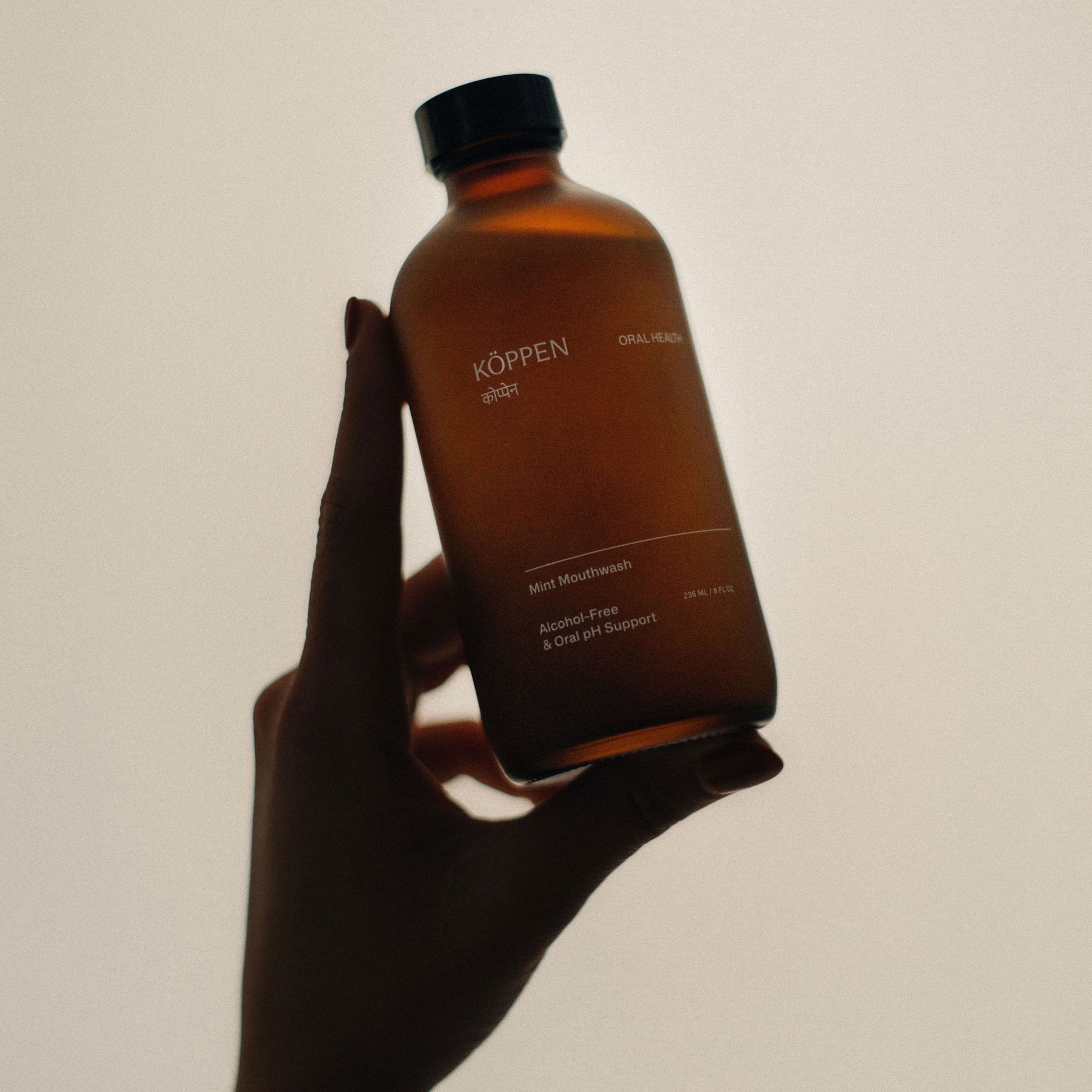 Hand holding a brown amber frosted bottle labeled 'Köppen' against a plain background