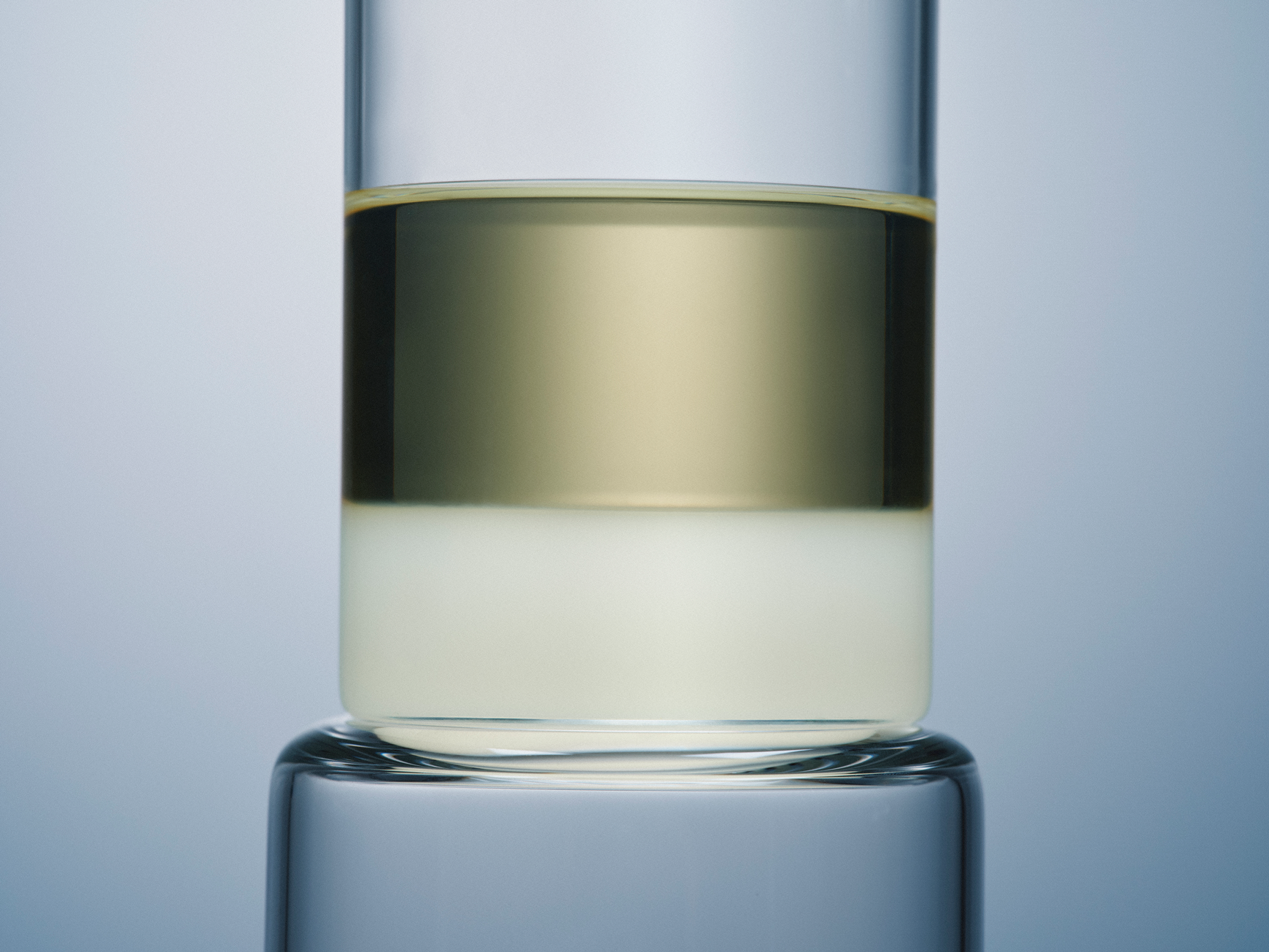 Glass container with a yellow oil and white liquid on a light blue background