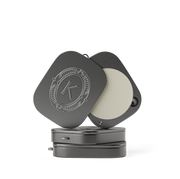 Grey lip balm compact with a lid featuring an embossed K logo on a white background