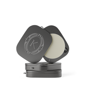 Grey lip balm compact with a lid featuring an embossed K logo on a white background