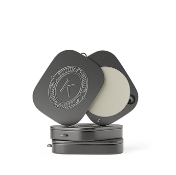 Grey lip balm compact with a lid featuring an embossed K logo on a white background