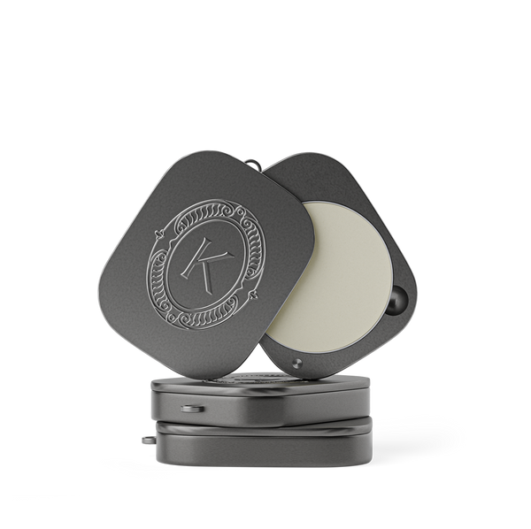 Grey lip balm compact with a lid featuring an embossed K logo on a white background