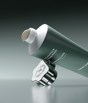 Green and white toothpaste tube with a silver cap on a gray background